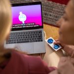 Two women watching an educational video on contraception and holding condoms indoors.