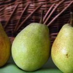 A detailed view of ripe pears placed in front of a woven wicker basket, capturing a rustic aesthetic.
